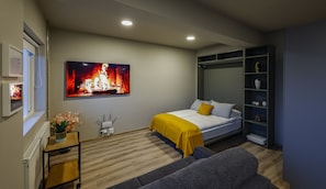 A bedroom with a bed, a sofa, a TV displaying a fireplace, and a wardrobe.