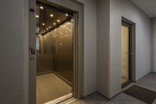 An elevator with a glass door, a control panel, and a fire alarm.