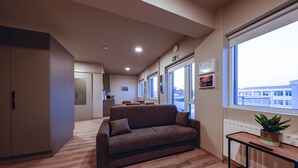 A modern hotel room with a sofa, a small table with a plant, and a view of the city through large windows. - Modern  apartment located in central Reykjavik. - Studio 3 (Reykjavík)
