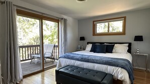 Une chambre avec un grand lit, une table de chevet, une fenêtre et un balcon équipé de chaises.