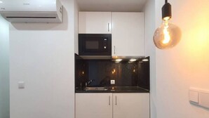 Een kleine keuken met witte kastjes, een zwart aanrecht, een magnetron en een hanglamp.