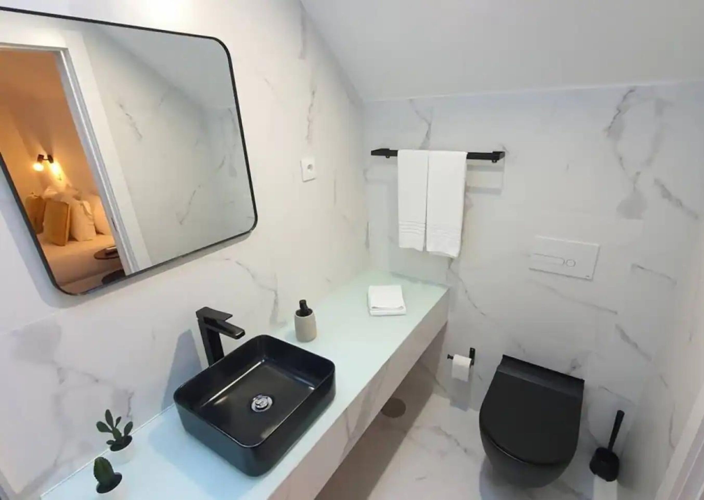 Et moderne badeværelse med en sort vask, et spejl, en håndklædestang og et toilet.