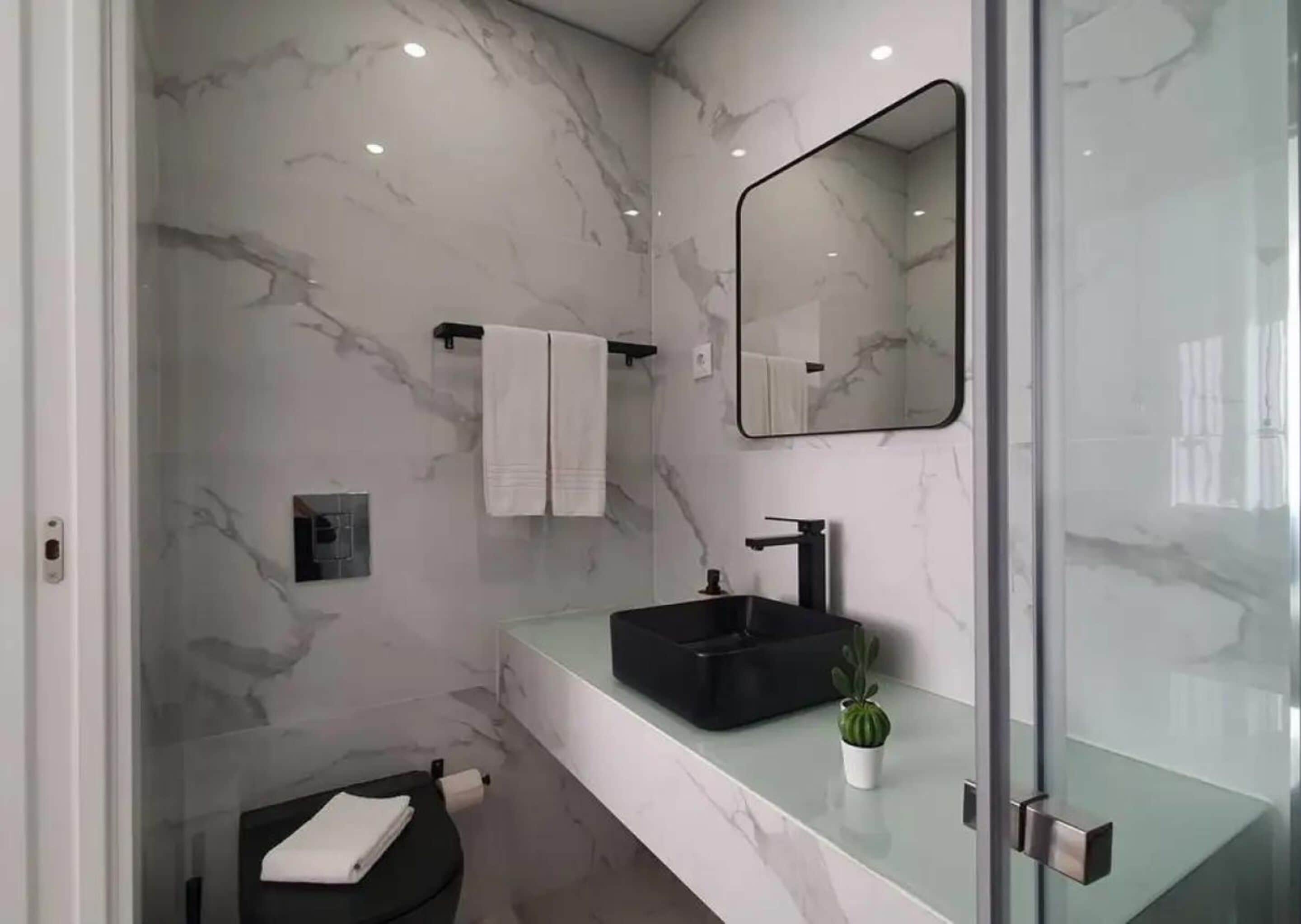 A modern bathroom with a marble wall, a black sink, a mirror, and a small potted plant.