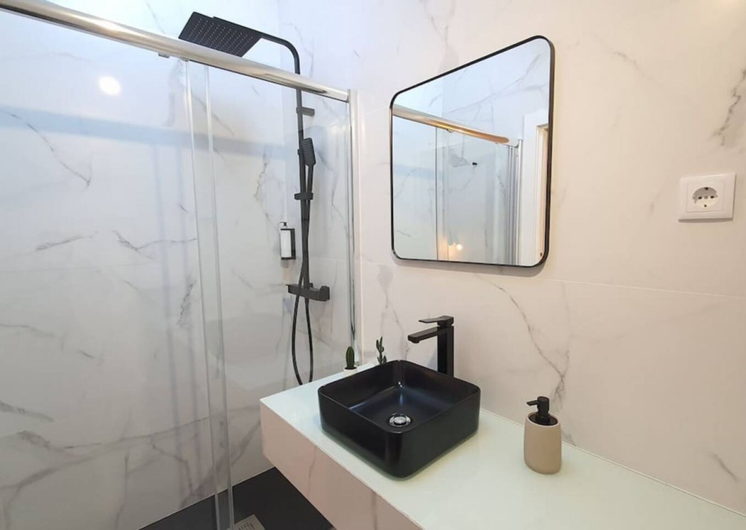 A modern bathroom with a glass shower enclosure, a black sink, and a mirror.