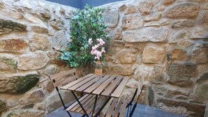 Een houten tafel met bankje tegen een stenen muur, met een bloempot en bloemen.