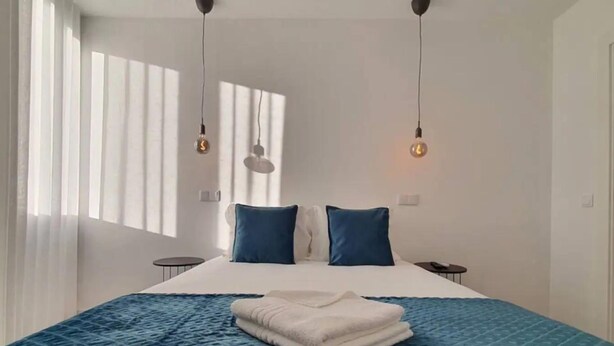 Een moderne hotelkamer met een groot bed, twee blauwe kussens, een witte deken en hanglampen.