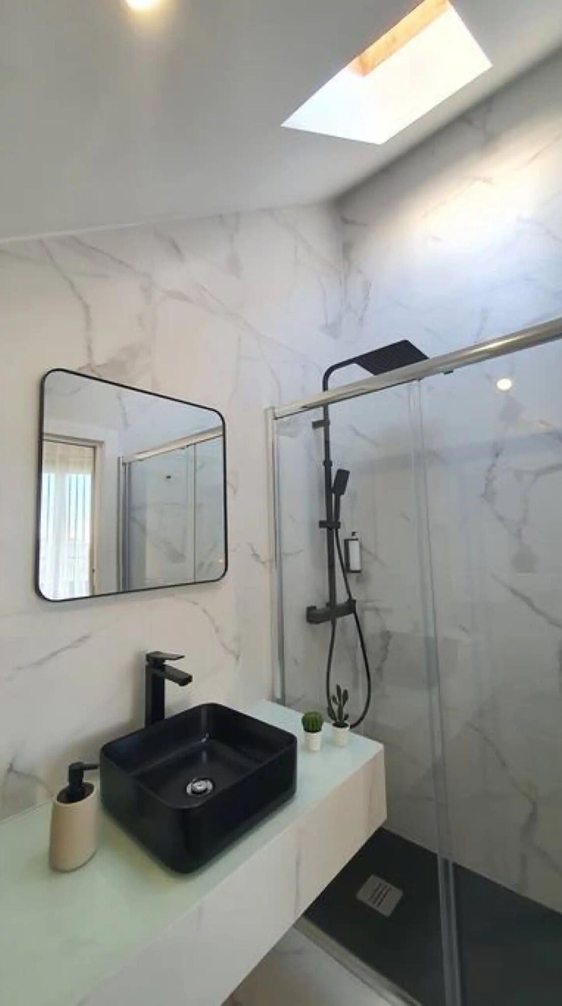 Une salle de bain moderne avec un mur en marbre, un lavabo noir, un miroir et une douche en verre.