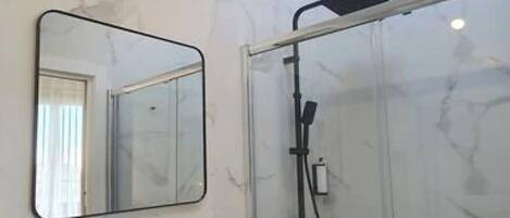 Une salle de bain moderne avec un mur en marbre, un lavabo noir, un miroir et une douche en verre.