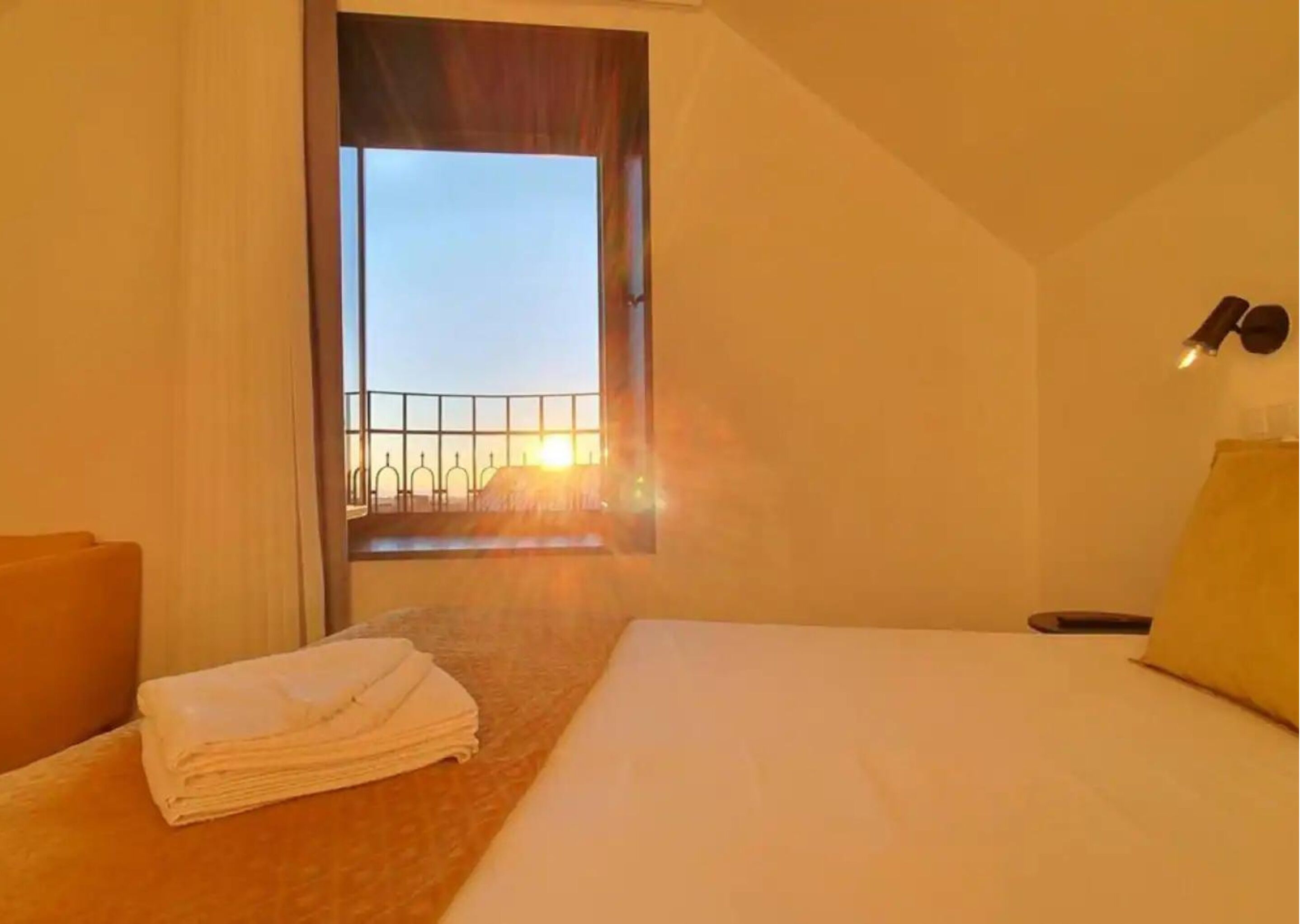 Una camera d'albergo con un letto, una sedia, una finestra vista balcone e un mucchio di asciugamani.
