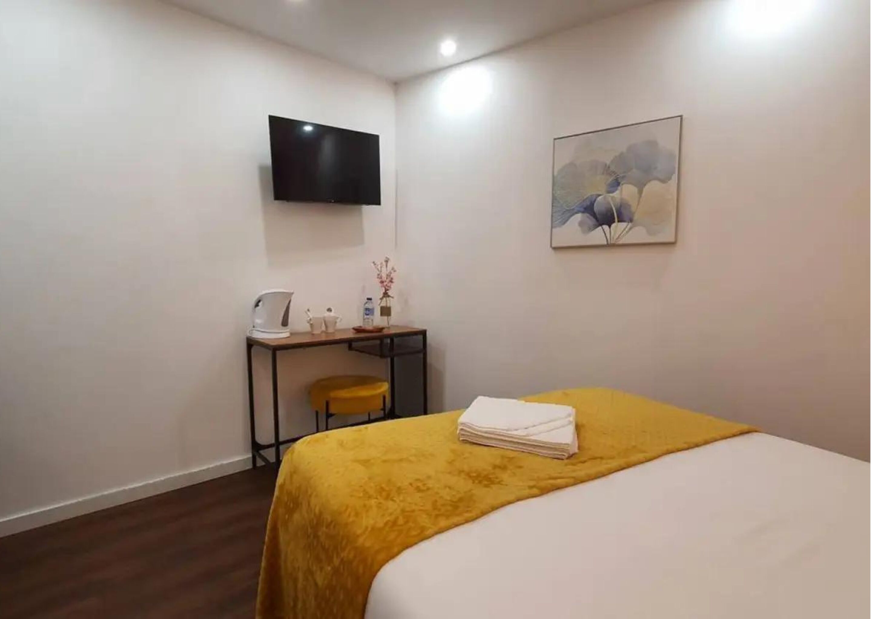 A hotel room with a bed, a desk with a chair, a flat-screen TV, and a painting on the wall.