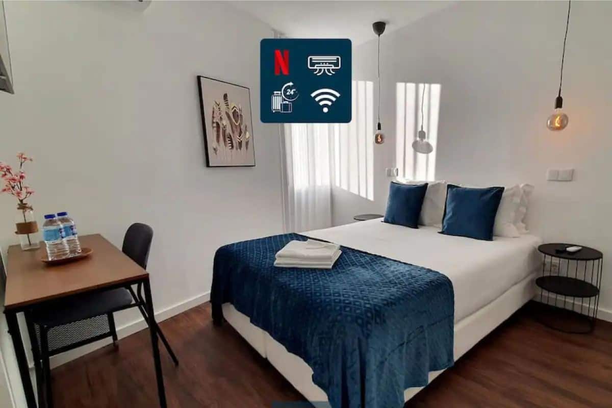 A modern hotel room with a neatly made bed, a small desk with a water bottle, and a picture on the wall.