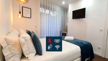 A modern hotel room with a neatly made bed, a flat-screen TV mounted on the wall, and a large window with vertical blinds.