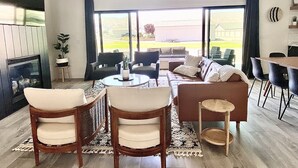 A spacious living room with a large sofa, two armchairs, a coffee table, and a dining area with chairs. There is a fireplace, a large window with a view of the outdoors, and a potted plant. - Modern Getaway with Community Pool near Golf, Boating & Gorge Concerts! (Mattawa)
