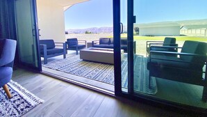 A modern living room with a sliding glass door leading to an outdoor patio with seating and a view of the mountains. - Modern Getaway with Community Pool near Golf, Boating & Gorge Concerts! (Mattawa)