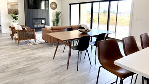 A modern living room with a sofa, dining table, and chairs. There is a fireplace, large windows, and a plant. - Modern Getaway with Community Pool near Golf, Boating & Gorge Concerts! (Mattawa)
