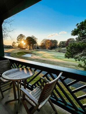 A balcony with a table and chairs overlooking a golf course during sunset. - Beautiful 1 bedroom condo with a view! (Williamsburg)