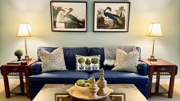 A living room with a blue sofa, two side tables with lamps, a coffee table with decorative items, and two framed wall art pieces.