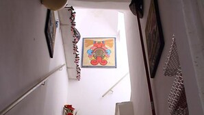 Een smalle trap met witte treden die omhoog leidt, een decoratieve wandversiering en een ingelijst foto bovenaan.