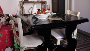 Een eetgedeelte met een zwarte tafel, witte stoelen, een fruitschaal en een hangende decoratie.