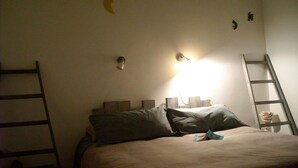 Een bed met kussens, een nachtkastje, een wandlamp en een ladder tegen de muur.