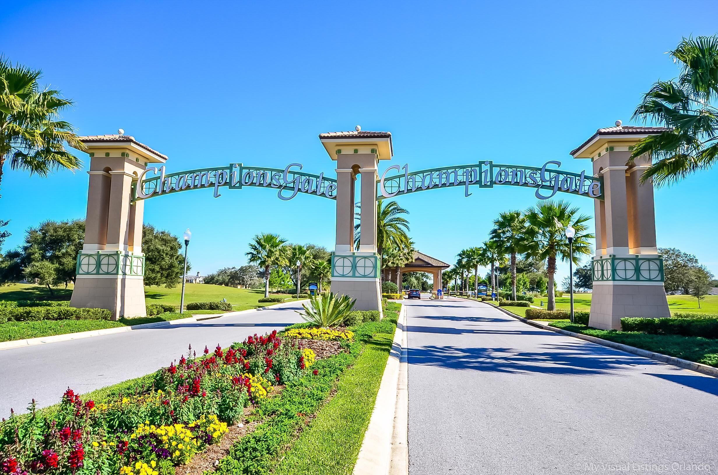 A gated entrance with a sign, palm trees, and a flower bed.