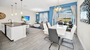 A modern kitchen with a central island, a dining area with a white table and chairs, and a living area with a sofa and a TV. - Gorgeous Townhouse on Resort Close To Disney (Davenport)