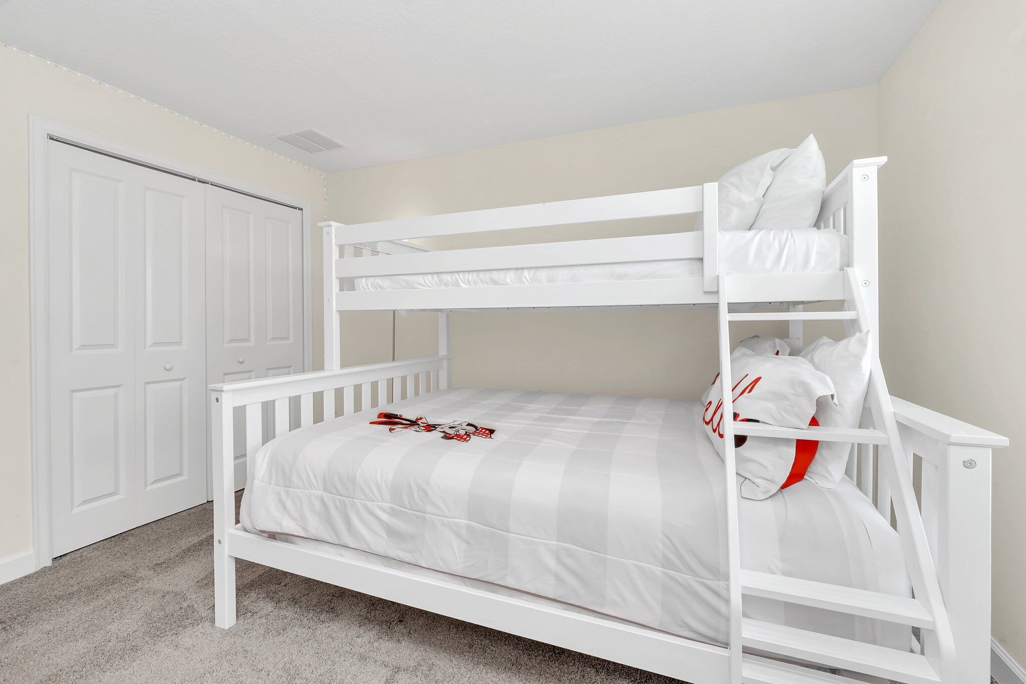 Una cama individual con ropa de cama blanca y un cojín rojo, una puerta blanca y suelo con alfombra.