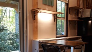 A compact kitchen with a wooden table, a black chair, and a window with a view of greenery. - Big Porch Tiny House (Brevard)