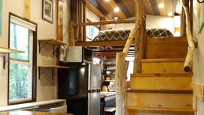A rustic interior with a wooden staircase, a kitchen area, and a dining space. - Big Porch Tiny House (Brevard)