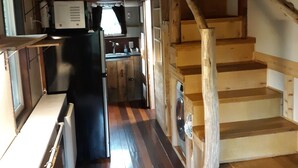 A compact kitchen with wooden floors, a built-in microwave, and a wooden staircase. - Big Porch Tiny House (Brevard)