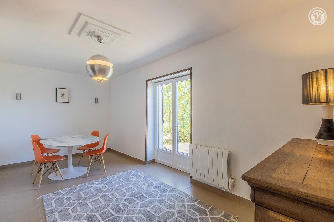 A modern room with a dining table and chairs, a radiator, a window, and a lamp.
