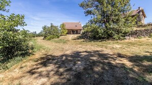 A rustic house with a stone wall and a wooden roof, surrounded by trees and a dry grassy field. - Thélème - Pouilloux - Gîte (POUILLOUX)