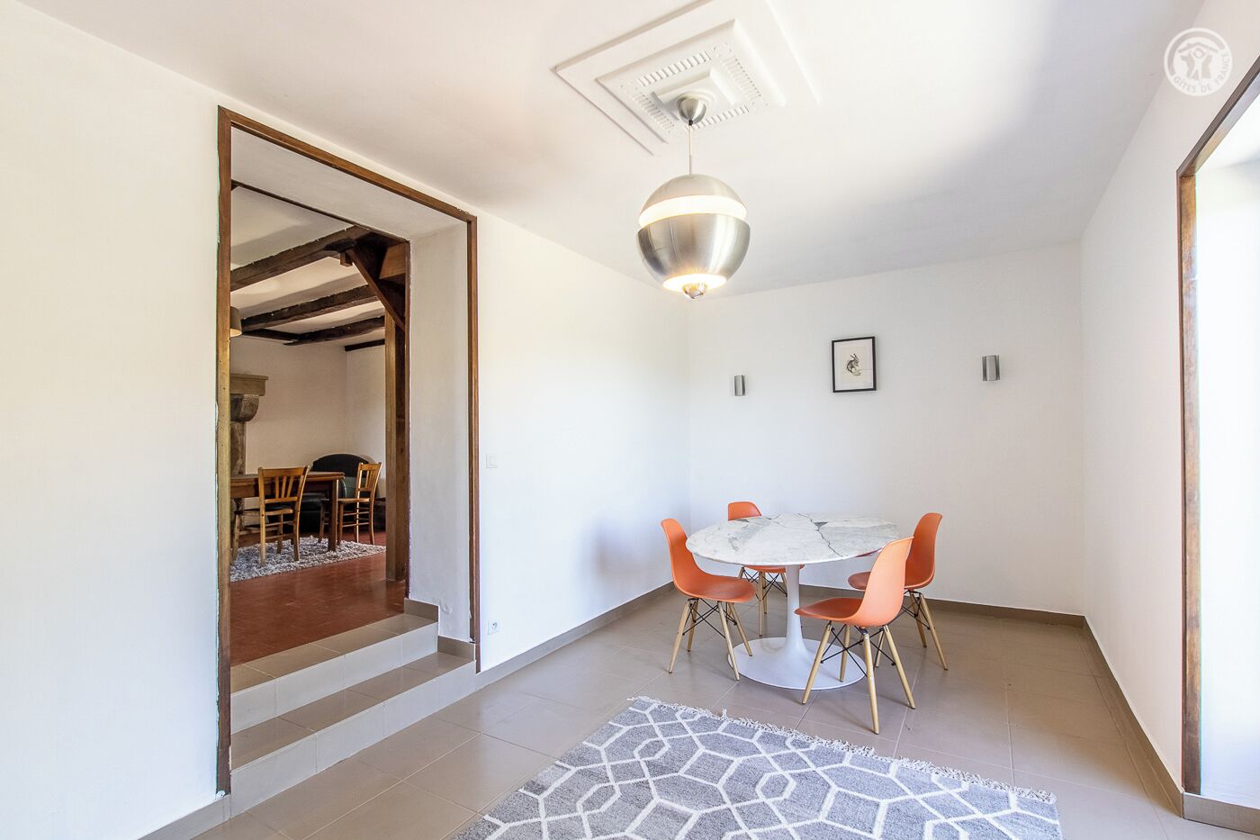 Un espace repas moderne avec une table ronde, des chaises orange et un sol à motifs de marbre.