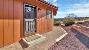 A wooden building with a dark door, a small window, and a brick pathway leading to a landscaped area. - Mountain Views + Deck | Near Lynx Lake (Prescott)