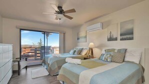 A bedroom with two beds, a ceiling fan, a large window with a view, and a small desk. - Mountain Views + Deck | Near Lynx Lake (Prescott)