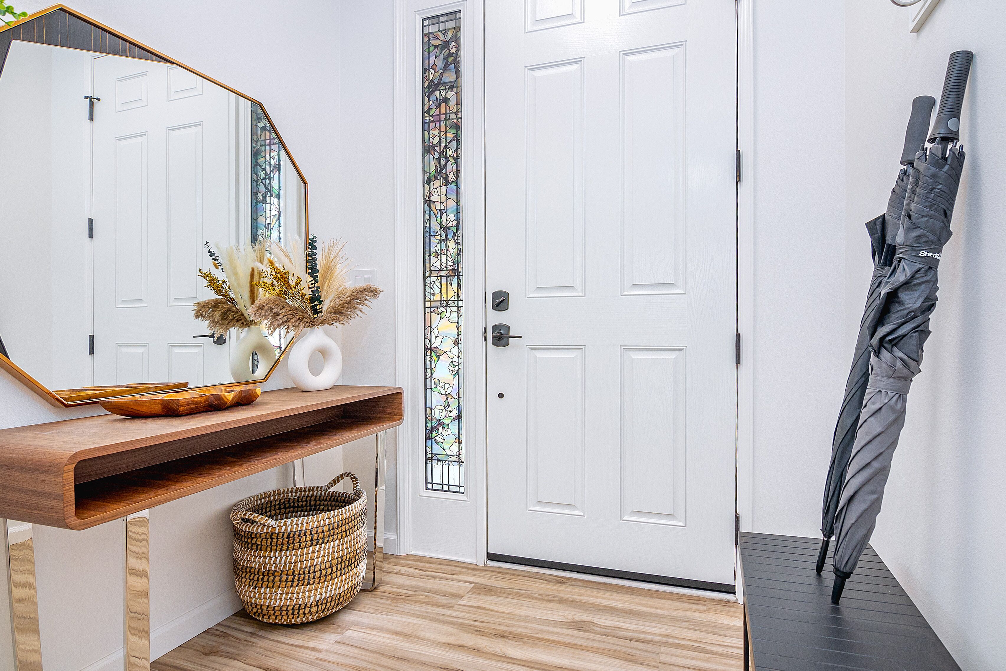 A hallway with a white door, a wooden console table with a mirror, a wicker basket, and a black umbrella leaning against the wall.