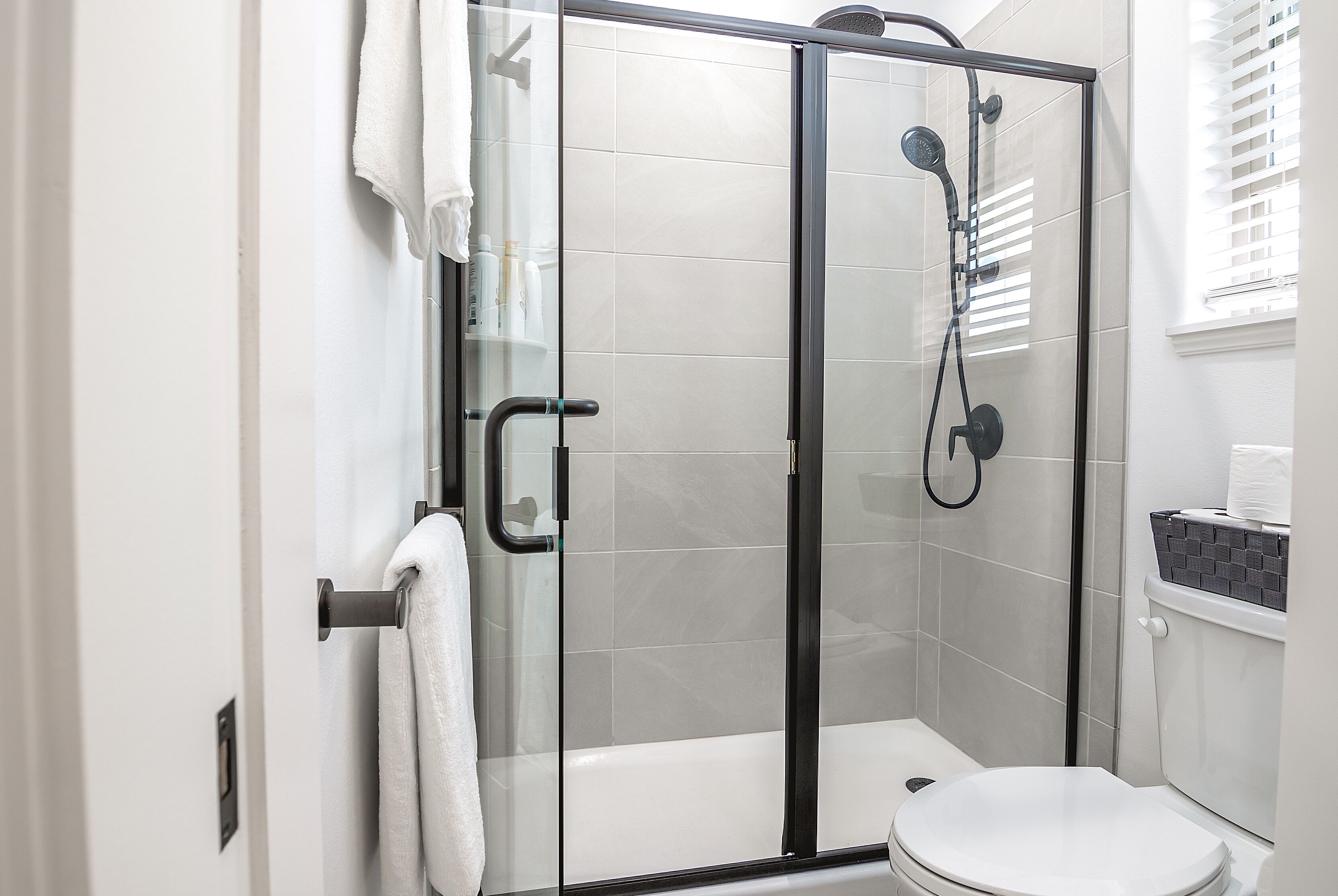 A glass-enclosed shower stall with a white toilet and a small window.