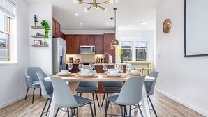 A modern kitchen with wooden cabinets, a stainless steel refrigerator, and a dining area with a table set for four. - New 4br home 5 min from the beach-Paradise escape (Waianae)