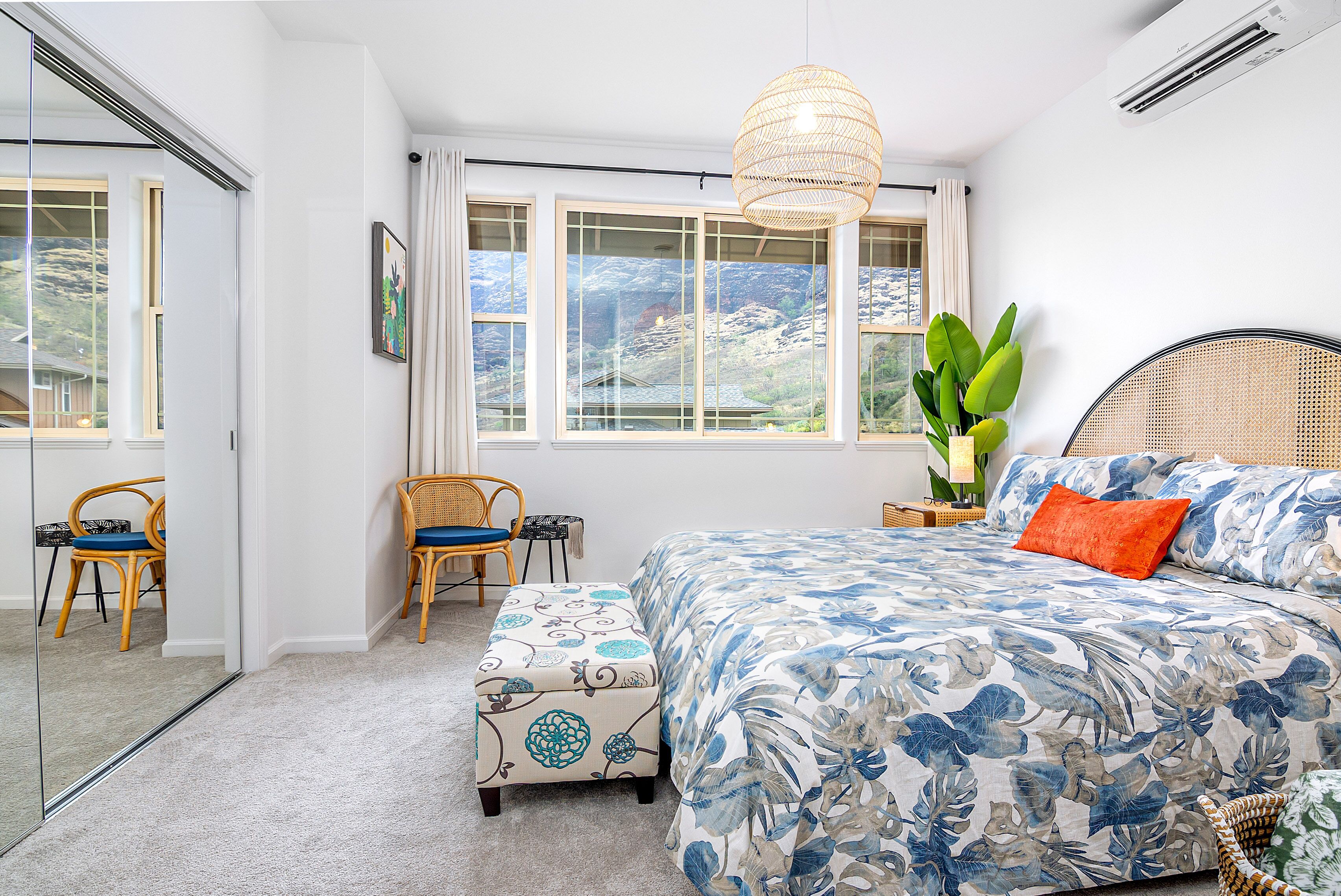 A bedroom with a large bed, a window with a view, a wicker chair, and a small table.