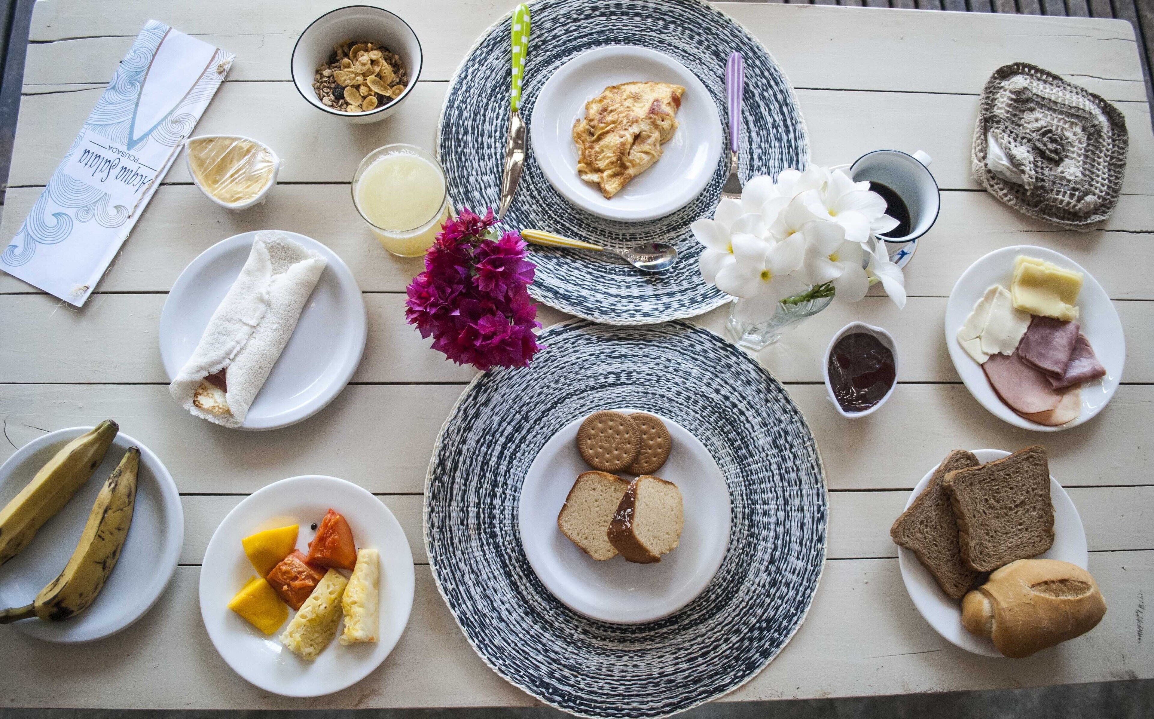 A breakfast setting with plates of toast, eggs, and fruit, along with a bowl of cereal and a cup of juice.
