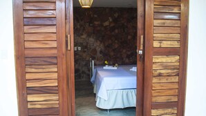 Ein Zimmer mit einer Steinwand, einem Bett mit weißer Bettdecke und Holztüren.