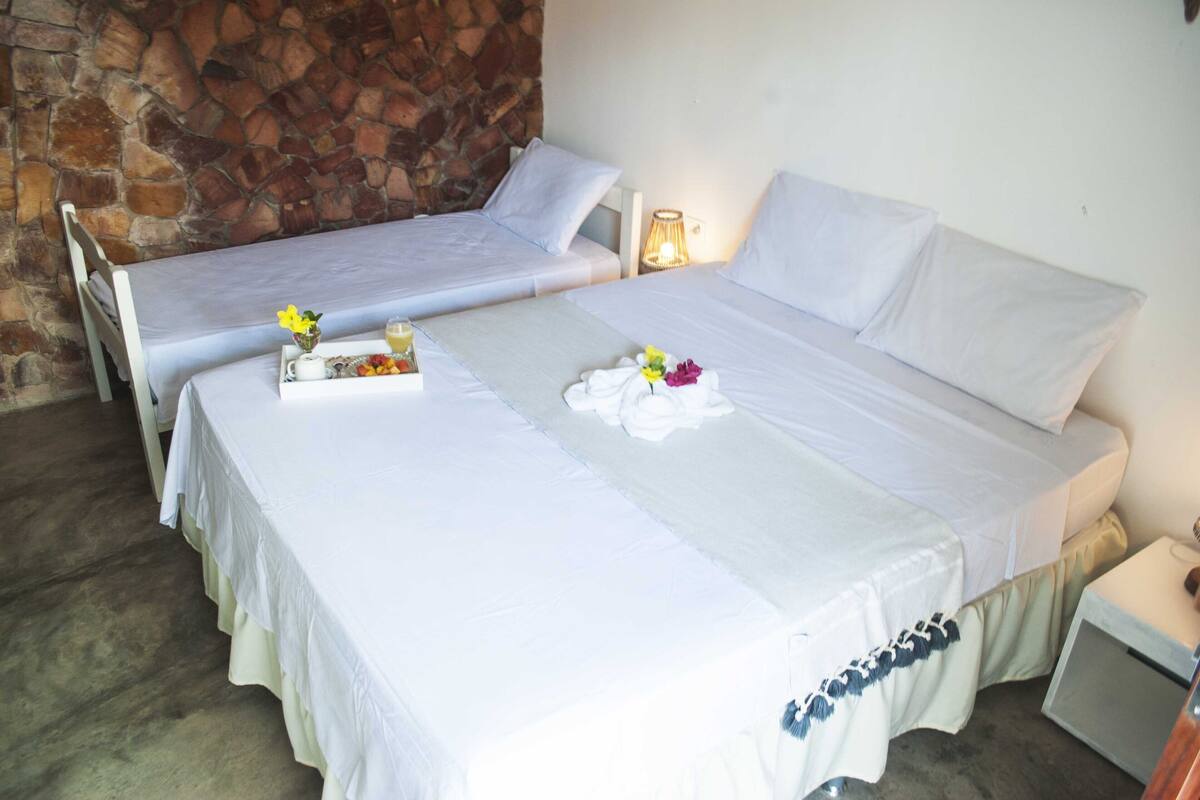 Habitación con dos camas, cada una con ropa blanca y almohadas, una bandeja con alimentos para el desayuno y una pared de piedra.