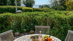 A wooden table with a bottle, fruits, and a bowl of flowers in a garden with a bench and a view of the sea. - Beautiful home in Samsø with WiFi (Samsø)