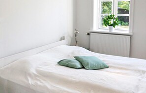 A bedroom with a bed, a radiator, a window with a view of greenery, and a plant on the windowsill. - Beautiful home in Samsø with WiFi (Samsø)