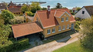 A yellow house with a red-tiled roof, surrounded by greenery and a view of a body of water. - Beautiful home in Samsø with WiFi (Samsø)