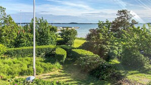 A landscaped garden with a water body in the background, a clear sky, and a distant shoreline. - Beautiful home in Samsø with WiFi (Samsø)