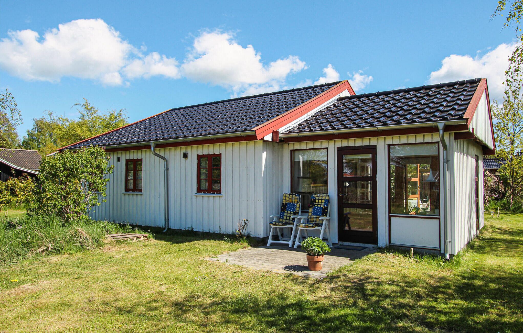 A single-story building with a tiled roof, a front porch with two chairs, and a small garden area.
