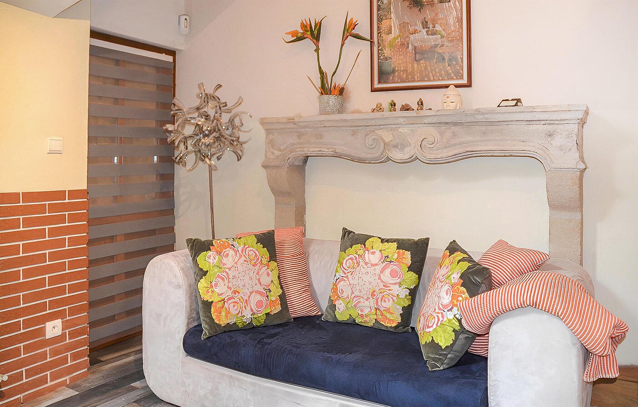 A living room with a white sofa, floral cushions, a decorative plant, and a framed painting above a fireplace.