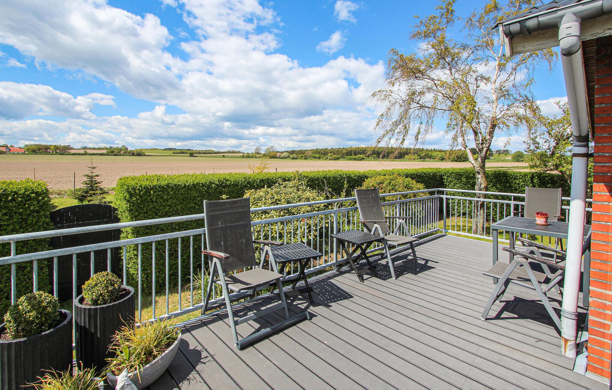 A deck with outdoor furniture, a view of a field, and a hedge.