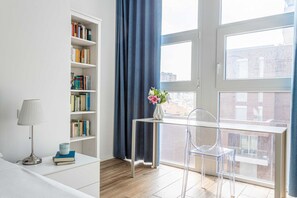 Habitación moderna con estantería, un escritorio con silla, lámpara y vistas por la ventana.